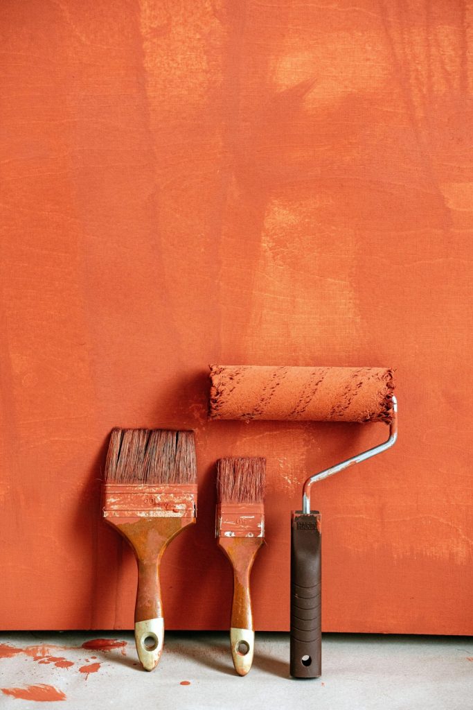 chetoi renovation toulouse pinceaux et rouleau de peinture posé sur un mur orange après utilisation