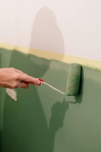 chetoi rénovation toulouse artisan en plein travail de peinture avec un rouleau sur un mur qu'il peint en vert sauge.