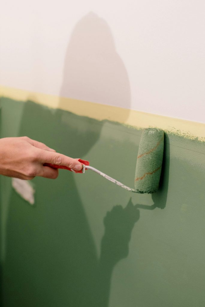 chetoi rénovation toulouse artisan en plein travail de peinture avec un rouleau sur un mur qu'il peint en vert sauge.
