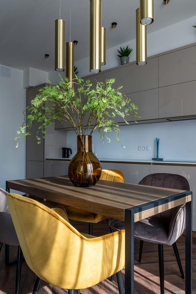 chetoi renovation toulouse salle à manger qui donne sur une cuisine beige moderne et tendances, avec table en bois et chaises en velours et plante posé en milieu de table