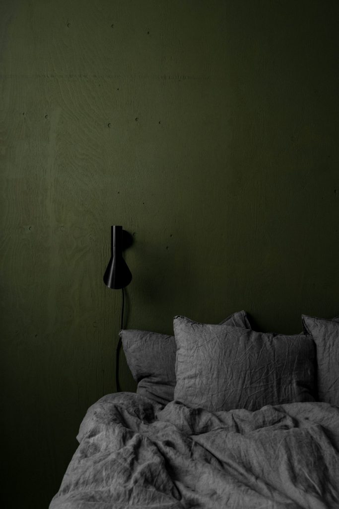 Lit aux draps gris devant un mur vert forêt, illustrant une chambre cosy aux couleurs tendance 2025.