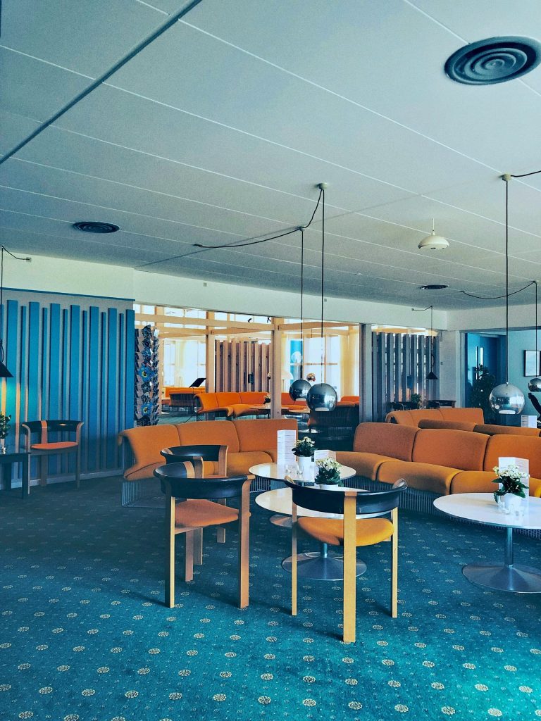 Intérieur rétro avec mobilier orange et tables rondes, rappelant l’influence vintage revisitée.